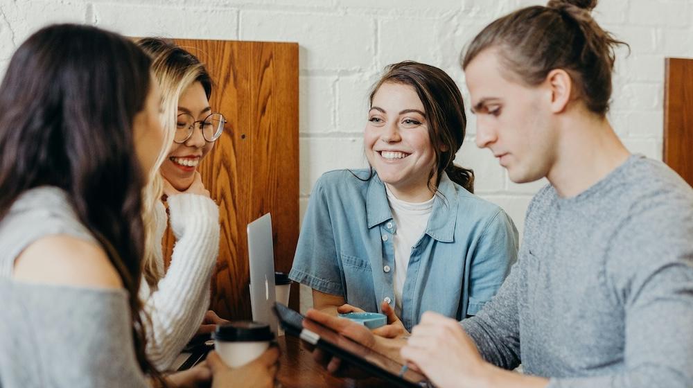 Four young people collaborating in a cafe with laptops